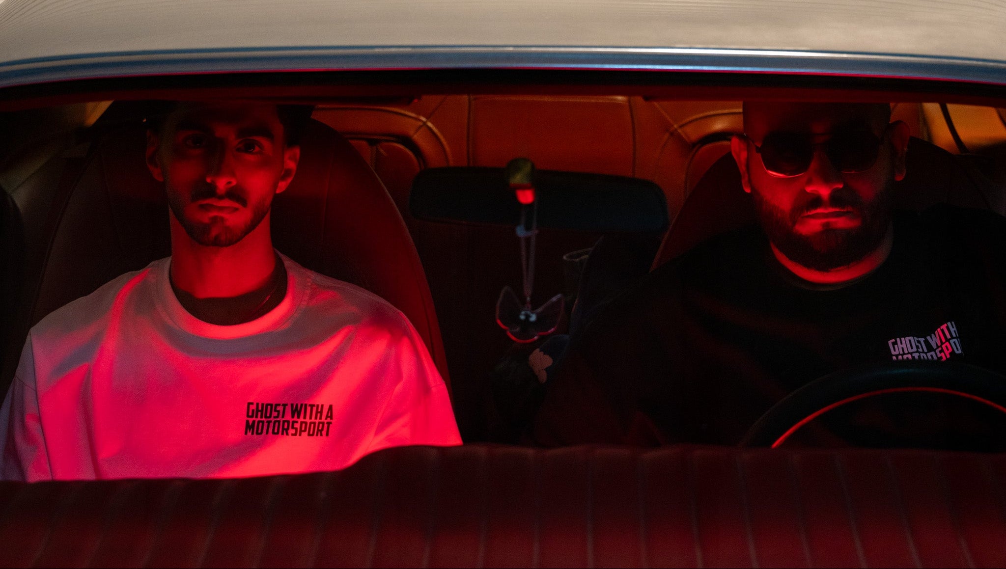 Two people sitting inside a car with a red light illuminating the interior.